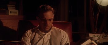 Movie still from “JFK” (1991), directed by Oliver Stone – A man sitting on top of a red couch wearing glasses; Close Up shot, Low angle