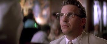 Movie still from “JFK” (1991), directed by Oliver Stone – A person wearing glasses and a suit; Close Up shot, Low angle