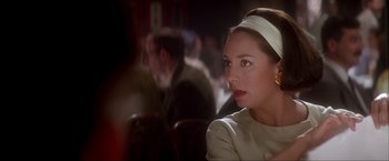 Movie still from “JFK” (1991), directed by Oliver Stone – A woman sitting at a table in front of a group of people; Close Up shot, Over the shoulder angle