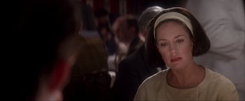 Movie still from “JFK” (1991), directed by Oliver Stone – A woman with a white headband is sitting at a table; Close Up shot, Over the shoulder angle