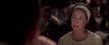 Movie still from “JFK” (1991), directed by Oliver Stone – A woman sitting in a room with a crowd of people in the background; Close Up shot, Over the shoulder angle