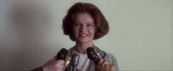 Movie still from “JFK” (1991), directed by Oliver Stone – A woman smiles while holding microphones in her hands; Close Up shot, Low angle