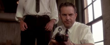 Movie still from “JFK” (1991), directed by Oliver Stone – A man in a white dress shirt and tie holding a camera; Close Up shot, Low angle