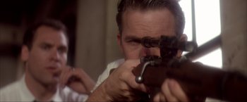 Movie still from “JFK” (1991), directed by Oliver Stone – A person holding a rifle; Close Up shot, Over the shoulder angle