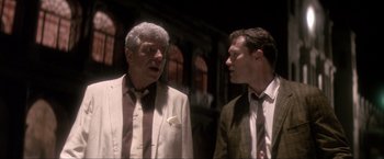 Movie still from “JFK” (1991), directed by Oliver Stone – Two men in suits talking to each other in a dark room; Medium shot, Over the shoulder angle