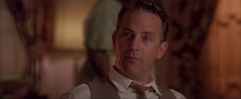 Movie still from “JFK” (1991), directed by Oliver Stone – A person wearing a suit and tie; Close Up shot, Over the shoulder angle