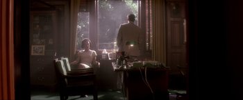 Movie still from “JFK” (1991), directed by Oliver Stone – A man and a woman are sitting in front of a window; Wide shot, Low angle