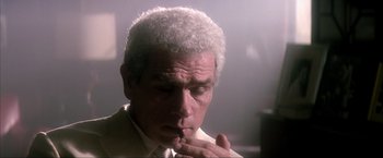 Movie still from “JFK” (1991), directed by Oliver Stone – An older man in a suit and tie smoking a cigarette; Close Up shot, Low angle
