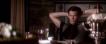 Movie still from “JFK” (1991), directed by Oliver Stone – A man sitting at a dinner table with his arms behind his head; Medium shot, Over the shoulder angle