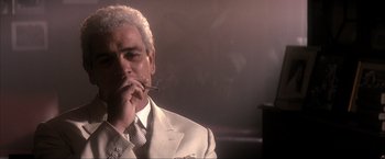 Movie still from “JFK” (1991), directed by Oliver Stone – An older man wearing a suit and tie smoking a cigarette; Close Up shot, Low angle