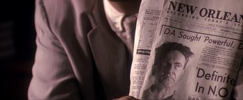 Movie still from “JFK” (1991), directed by Oliver Stone – A man in a suit and tie holding a newspaper; Extreme Close Up shot, Low angle
