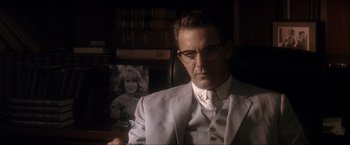 Movie still from “JFK” (1991), directed by Oliver Stone – A man in a suit and tie in front of a picture of a woman; Close Up shot, Over the shoulder angle