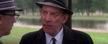 Movie still from “JFK” (1991), directed by Oliver Stone – An older man wearing a hat and a suit; Close Up shot, Over the shoulder angle