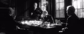 Movie still from “JFK” (1991), directed by Oliver Stone – Two men are sitting at a dinner table with candles lit; Medium shot, Over the shoulder angle