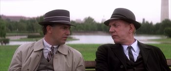 Movie still from “JFK” (1991), directed by Oliver Stone – A couple of men sitting next to each other on a park bench; Medium shot, Over the shoulder angle