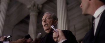 Movie still from “JFK” (1991), directed by Oliver Stone – An older man holding a microphone and a cell phone; Close Up shot, Low angle