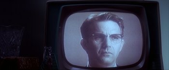 Movie still from “JFK” (1991), directed by Oliver Stone – A man with glasses is on a television screen; Close Up shot, Over the shoulder angle