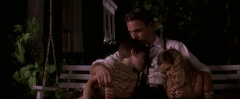 Movie still from “JFK” (1991), directed by Oliver Stone – A man sitting on a bench with two children; Medium shot, Low angle