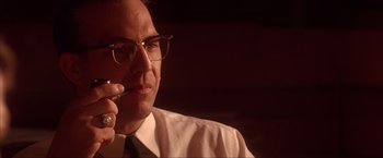Movie still from “JFK” (1991), directed by Oliver Stone – A man wearing glasses is holding a pen in his mouth; Close Up shot, Low angle