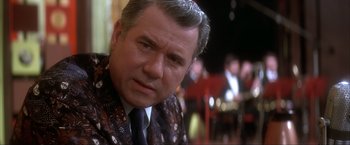 Movie still from “JFK” (1991), directed by Oliver Stone – An older man in a suit and tie looking to his left; Close Up shot, Over the shoulder angle