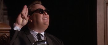 Movie still from “JFK” (1991), directed by Oliver Stone – A person wearing a suit and sunglasses; Close Up shot, Low angle