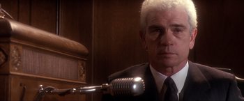 Movie still from “JFK” (1991), directed by Oliver Stone – A man in a suit with a microphone in front of him; Close Up shot, Low angle