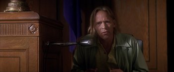 Movie still from “JFK” (1991), directed by Oliver Stone – A man sitting in front of a microphone in a dark room; Close Up shot, Low angle