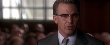 Movie still from “JFK” (1991), directed by Oliver Stone – A person wearing a suit and glasses; Close Up shot, Over the shoulder angle