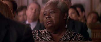 Movie still from “JFK” (1991), directed by Oliver Stone – An older woman sitting in front of a group of people; Close Up shot, Low angle