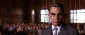 Movie still from “JFK” (1991), directed by Oliver Stone – A person wearing a suit and glasses; Close Up shot, Low angle