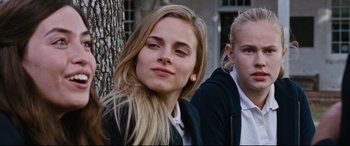 Movie still from “Jack Reacher: Never Go Back” (2016), directed by Edward Zwick – Two young women sitting next to each other near a tree; Close Up shot, Over the shoulder angle