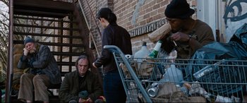 Movie still from “Jack Reacher: Never Go Back” (2016), directed by Edward Zwick – A group of people sitting on the steps of a brick building; Wide shot, High angle