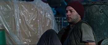 Movie still from “Jack Reacher: Never Go Back” (2016), directed by Edward Zwick – A man sitting on the ground wearing a red hat; Close Up shot, High angle