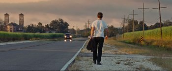 Movie still from “Jack Reacher: Never Go Back” (2016), directed by Edward Zwick – A man walking down the side of the road holding a bag; Wide shot, Over the shoulder angle