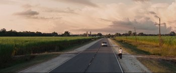 Movie still from “Jack Reacher: Never Go Back” (2016), directed by Edward Zwick – A man standing on the side of a road next to a white car; Extreme Wide shot, Over the shoulder angle