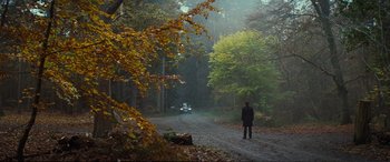 Movie still from “Jack Ryan: Shadow Recruit” (2014), directed by Kenneth Branagh – A man standing on a dirt road in the middle of a forest; Extreme Wide shot, Over the shoulder angle