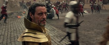 Movie still from “Jack the Giant Slayer” (2013), directed by Bryan Singer – A man in a gold and black outfit standing in front of a group of people; Close Up shot, Over the shoulder angle