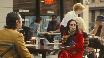 Movie still from “Jackass Forever” (2022), directed by Jeff Tremaine – A woman sitting at an outdoor table with a dog; Medium shot, Over the shoulder angle