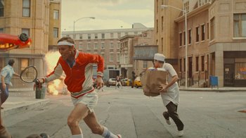Movie still from “Jackass Forever” (2022), directed by Jeff Tremaine – Two people running down a street with a bag of food; Wide shot, Low angle