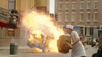 Movie still from “Jackass Forever” (2022), directed by Jeff Tremaine – A person holding a bag in front of a car on fire; Wide shot, Over the shoulder angle