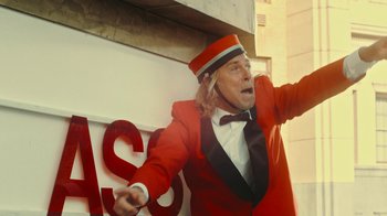 Movie still from “Jackass Forever” (2022), directed by Jeff Tremaine – A man dressed in a red suit and a red hat; Medium shot, Low angle