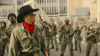 Movie still from “Jackass Forever” (2022), directed by Jeff Tremaine – A group of men in military uniforms marching down a street; Medium shot, Over the shoulder angle