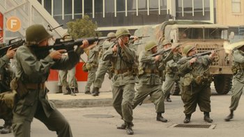 Movie still from “Jackass Forever” (2022), directed by Jeff Tremaine – A group of men in military fatigues marching down a street; Wide shot, High angle