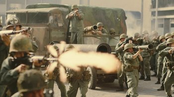 Movie still from “Jackass Forever” (2022), directed by Jeff Tremaine – A group of men in military fatigues and helmets are standing in front of an armored vehicle; Wide shot, Over the shoulder angle