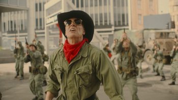 Movie still from “Jackass Forever” (2022), directed by Jeff Tremaine – A man wearing a cowboy hat and sunglasses while standing in front of a group of soldiers; Medium shot, Low angle
