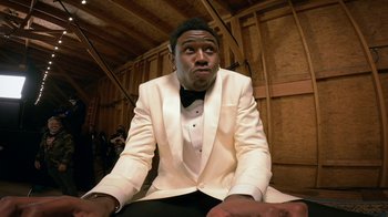 Movie still from “Jackass Forever” (2022), directed by Jeff Tremaine – A man in a white tuxedo sitting in a room; Medium shot, Low angle