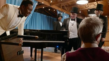 Movie still from “Jackass Forever” (2022), directed by Jeff Tremaine – A group of men standing next to each other in front of a grand piano; Medium shot, Over the shoulder angle