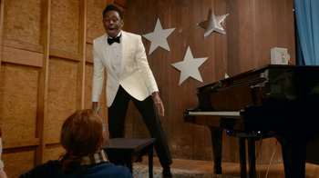 Movie still from “Jackass Forever” (2022), directed by Jeff Tremaine – A man in a white tuxedo standing in front of a piano; Medium shot, Over the shoulder angle