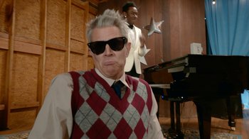 Movie still from “Jackass Forever” (2022), directed by Jeff Tremaine – A man wearing a red argyle vest and sunglasses; Medium shot, Over the shoulder angle