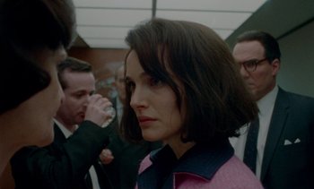 Movie still from “Jackie” (2016), directed by Pablo Larraín – A woman in a pink shirt and some people in the background; Close Up shot, Over the shoulder angle
